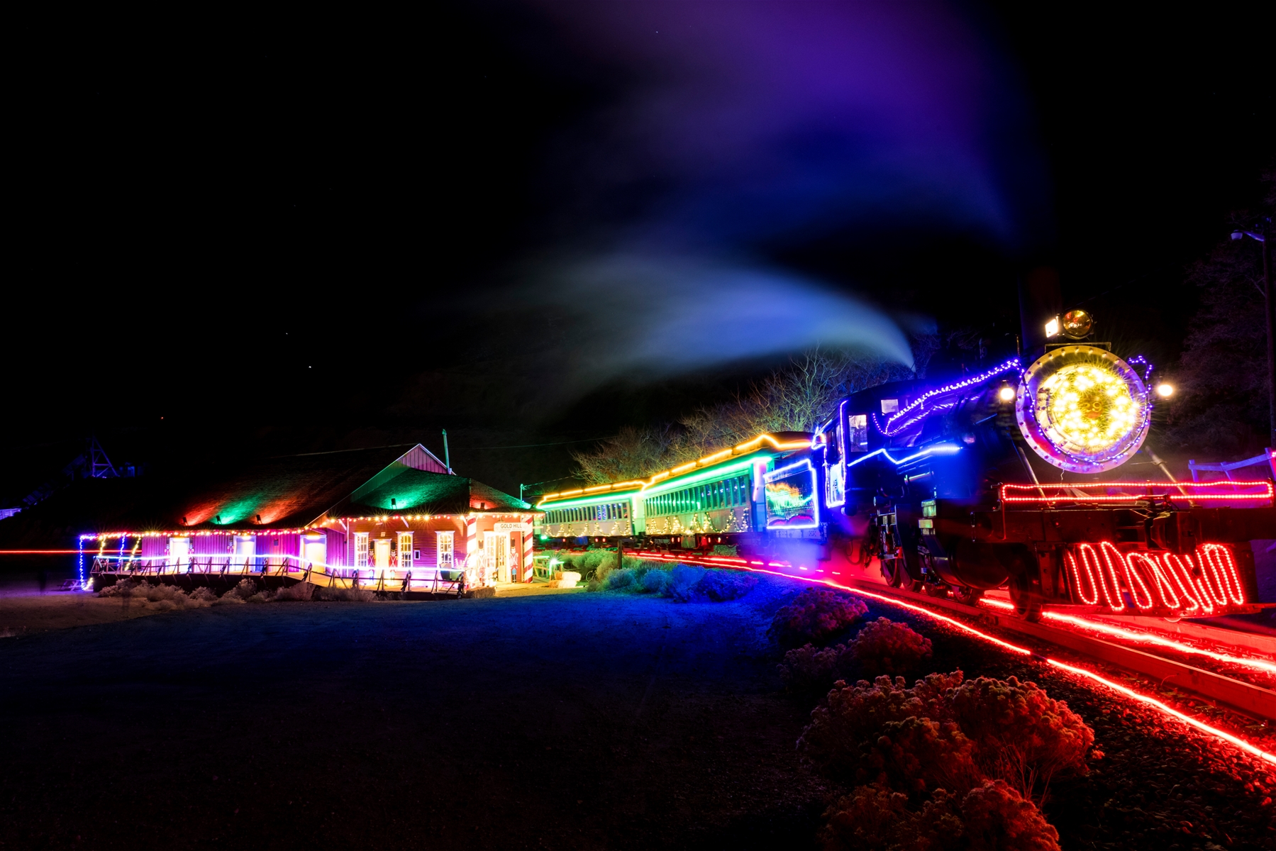 Holiday Steam Engine Covered In Lights On A Neon Train Track In The Dark